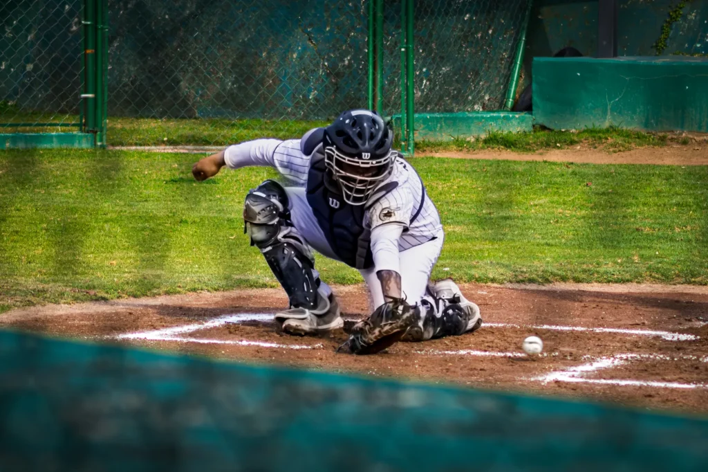 Receptor de béisbol con casco y peto se agacha para detener una pelota en el suelo, frente al plato